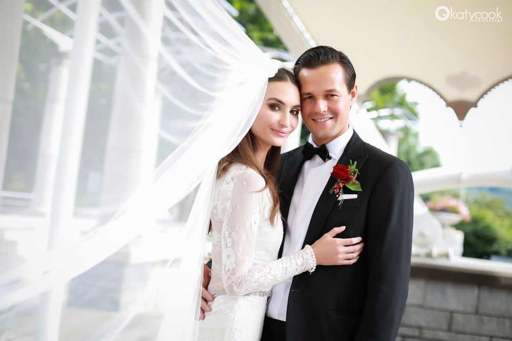 A romantic wedding portrait with flowing veil against a light architectural background.