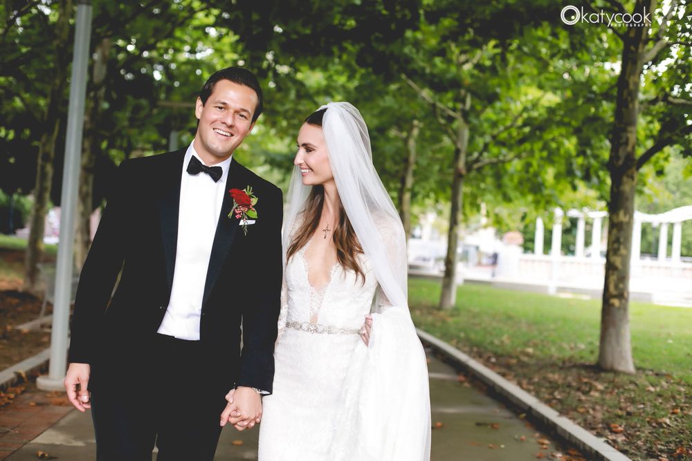 A joyful wedding couple walking hand in hand through a tree-lined pathway.