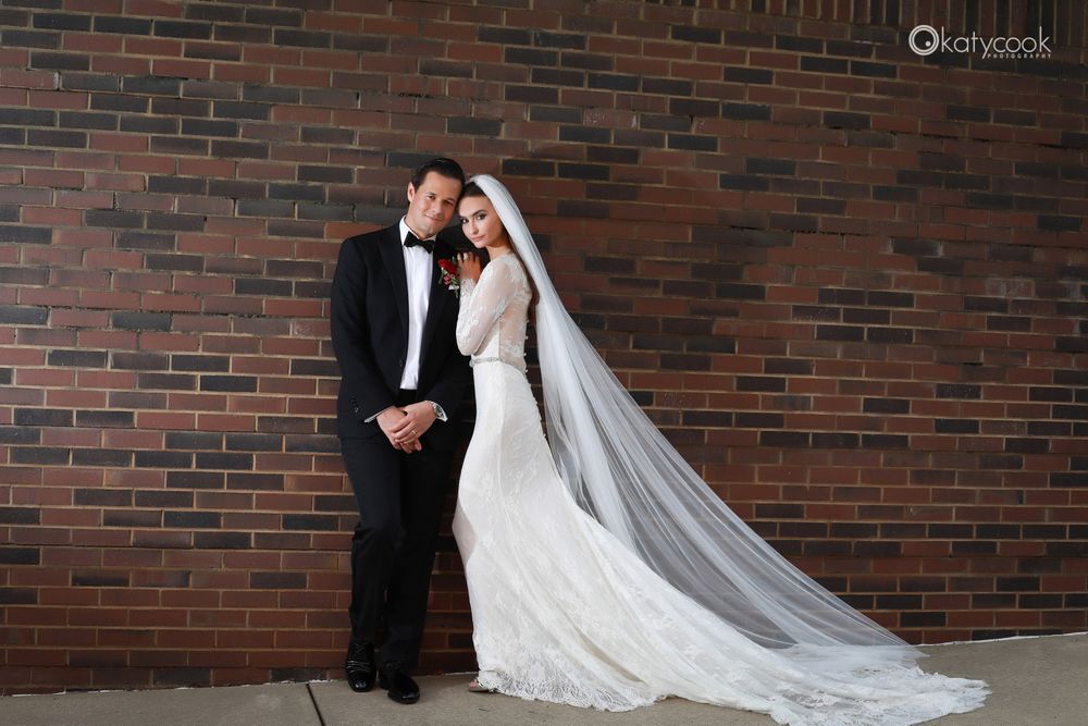 Intimate wedding portrait against textured brick wall with flowing veil detail.