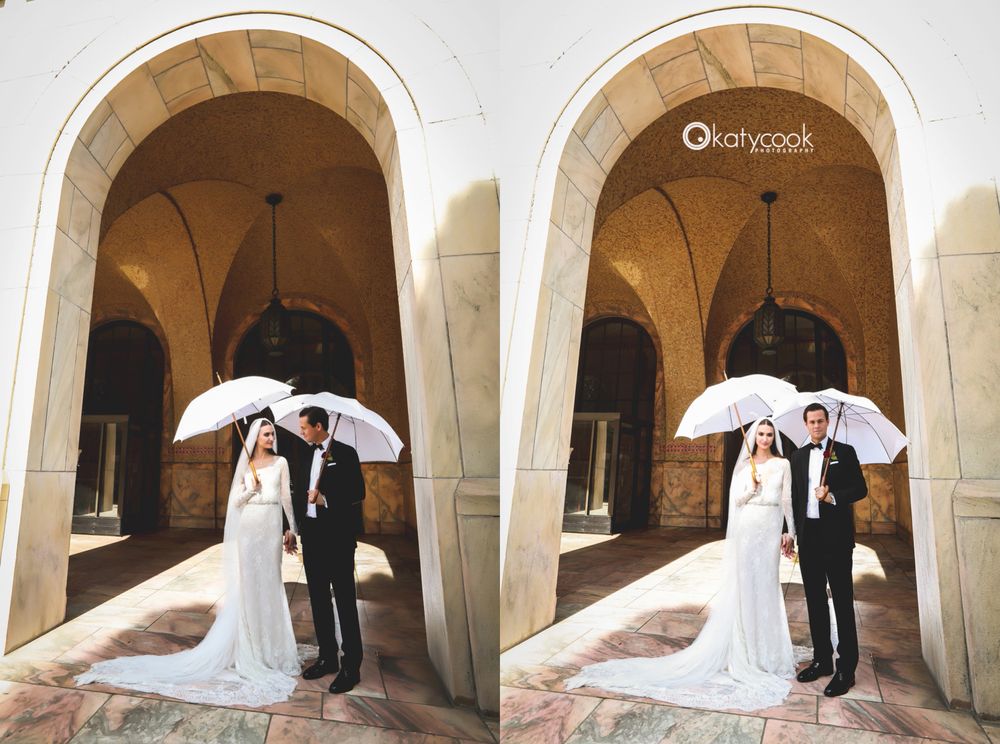 Wedding couple poses creatively with white umbrellas under stone archways.