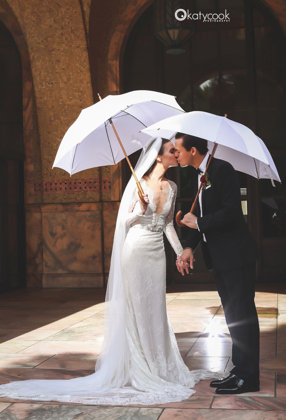 Wedding couple shares intimate moments under white umbrellas in an arched courtyard.