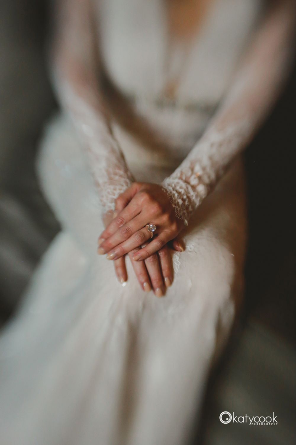 Close-up of lace wedding dress details and clasped hands with ring.