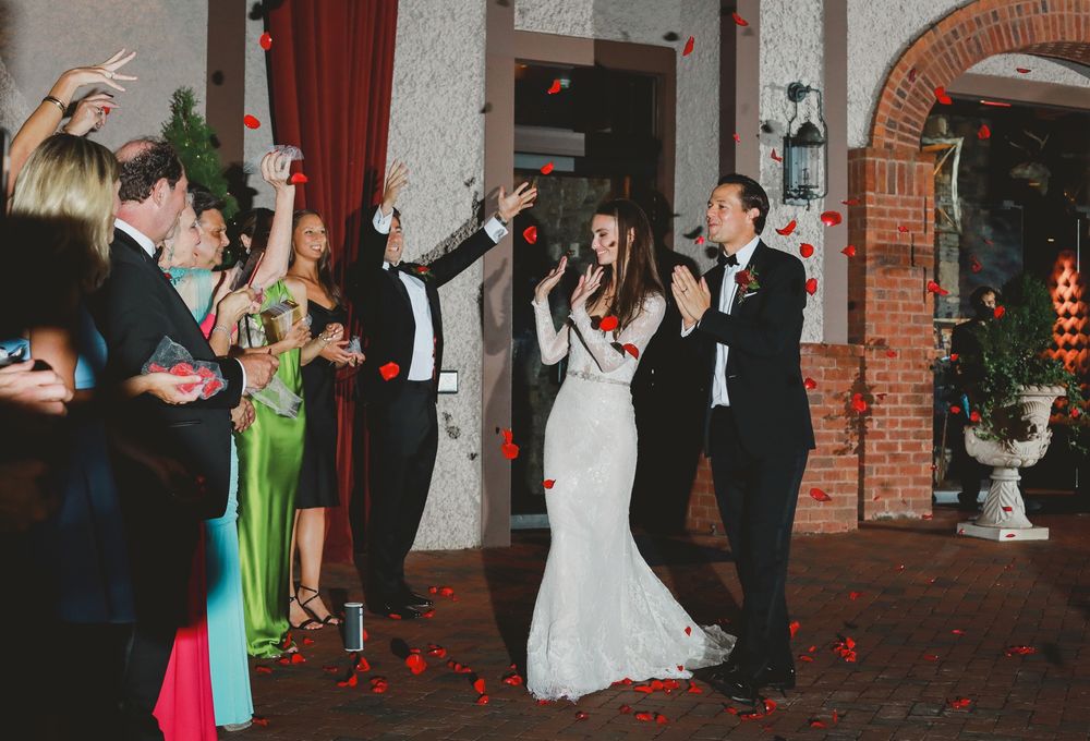 Wedding guests dance and celebrate in a rustic brick-walled venue with red curtains.