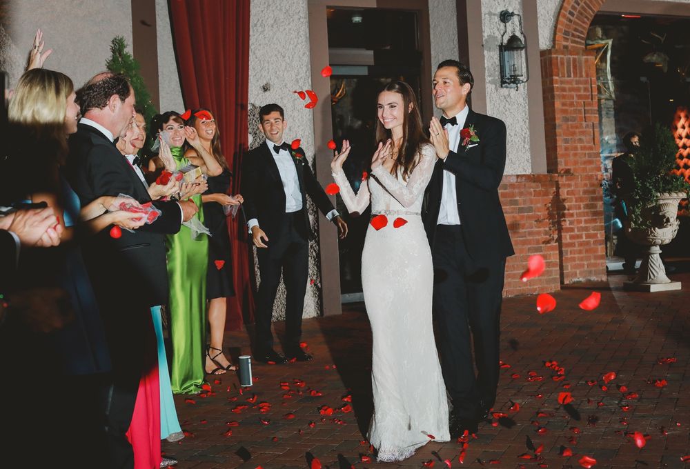 Wedding party celebrates with dancing in an elegant indoor venue decorated with red rose petals.