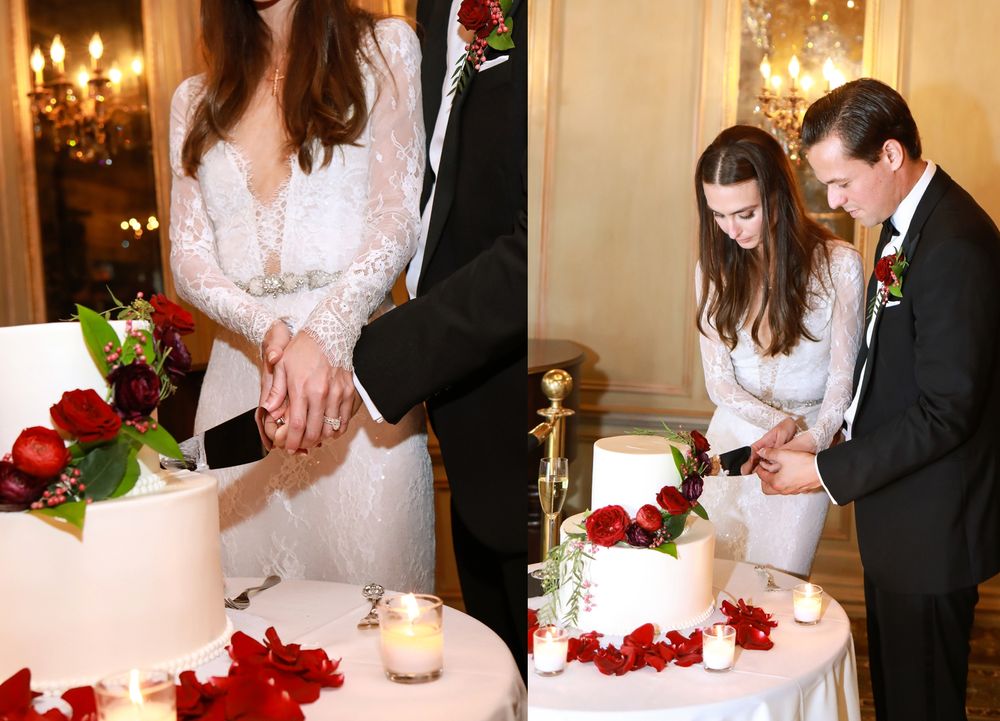 Newlyweds cutting their white wedding cake decorated with red rose petals.