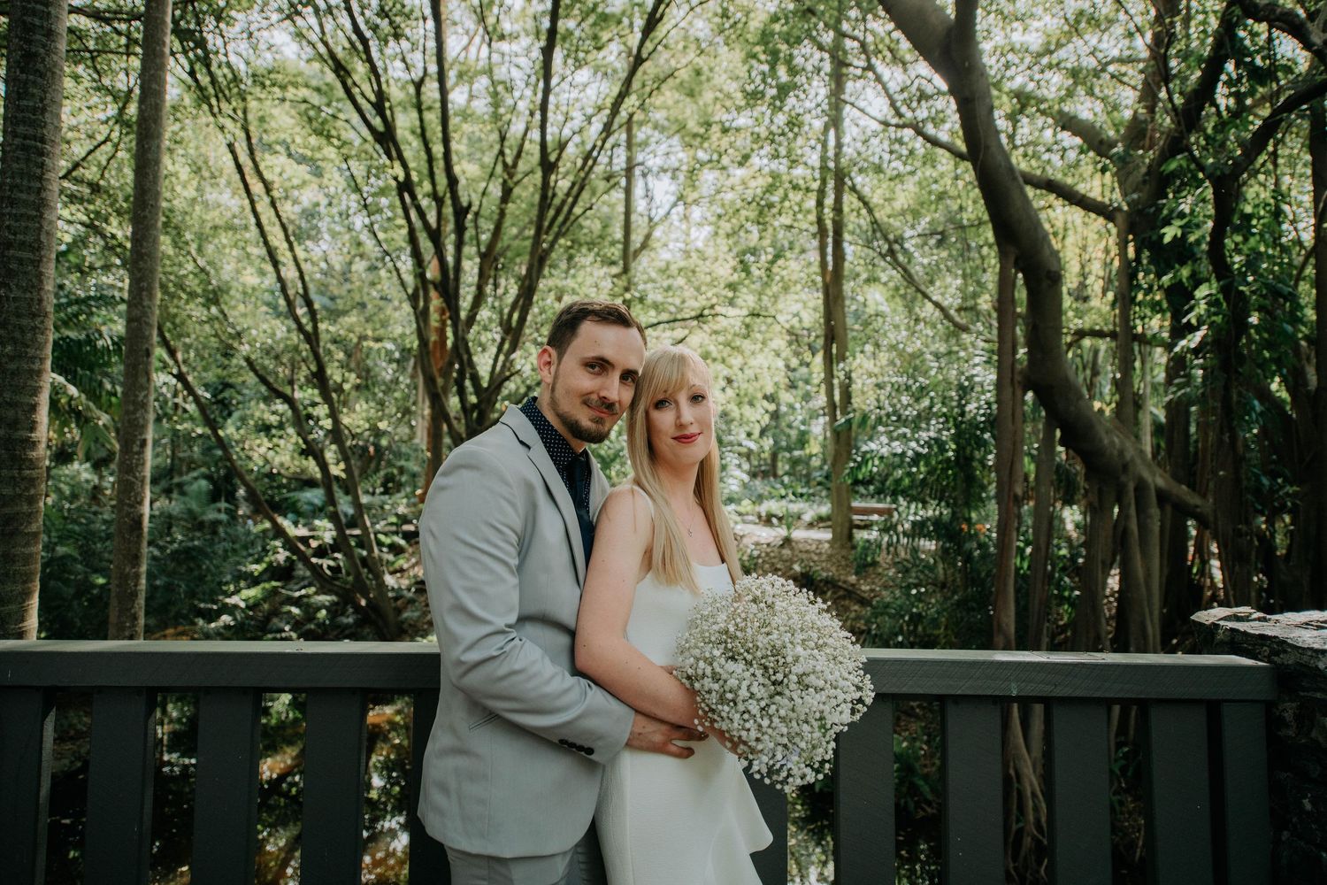 Romantic couple poses on wooden deck surrounded by lush forest greenery.