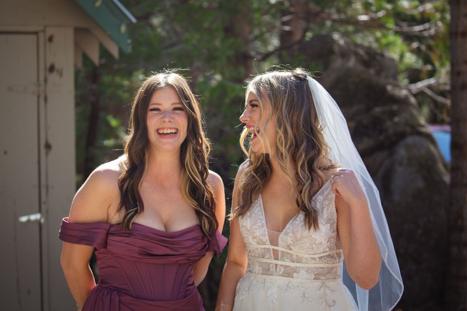 Two women in burgundy and white dresses laugh together during an outdoor celebration.