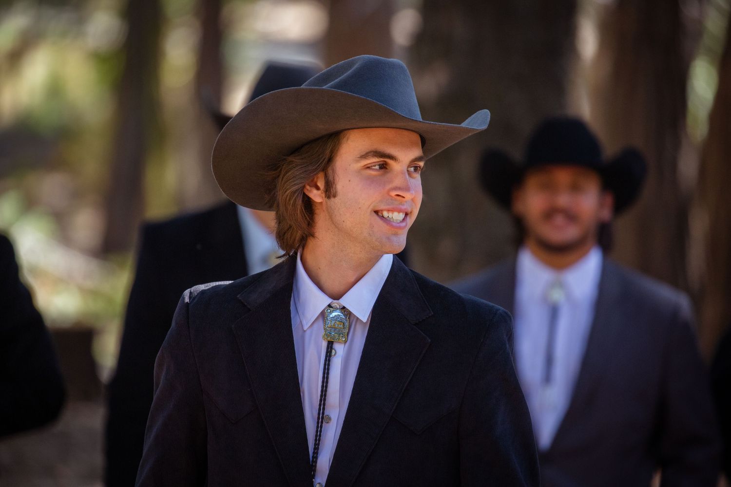 A person in a cowboy hat and suit jacket smiles while posing outdoors in multiple similar shots.