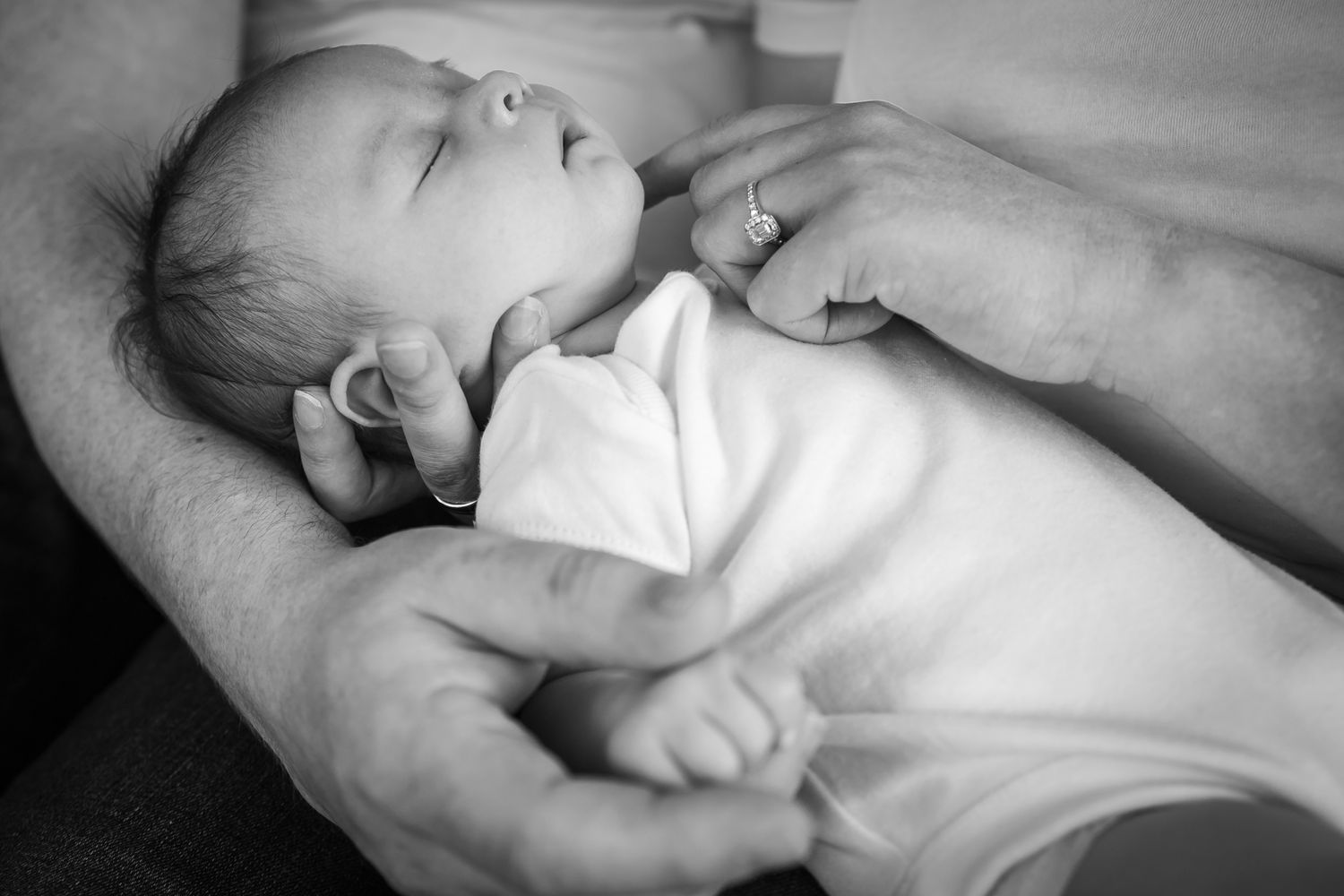 Sleeping baby in white clothes resting on adult's arm in monochrome.