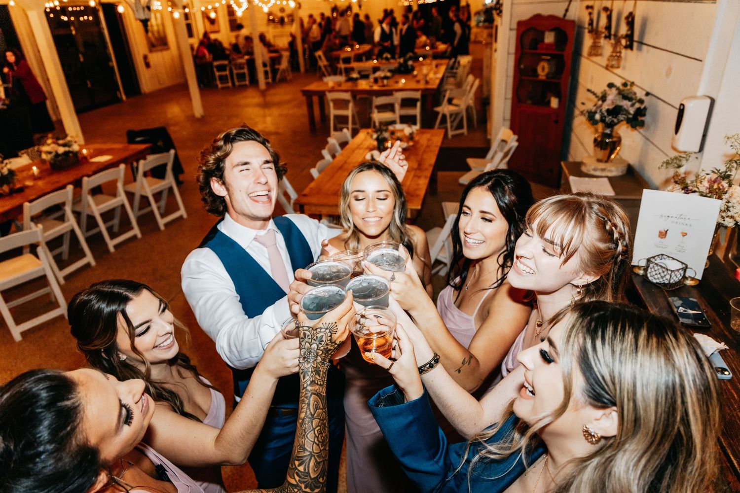 Wedding guests raise glasses in a joyful champagne toast during a lively indoor reception celebration.