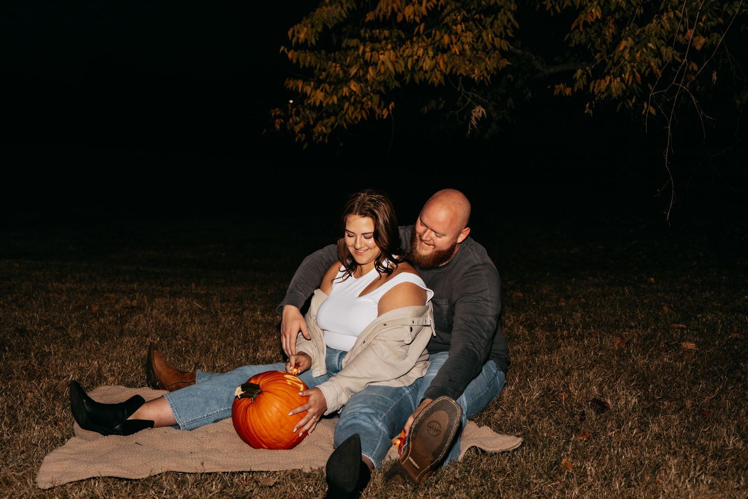 Couple sitting on a blanket at night with a pumpkin during a fall engagement session.
