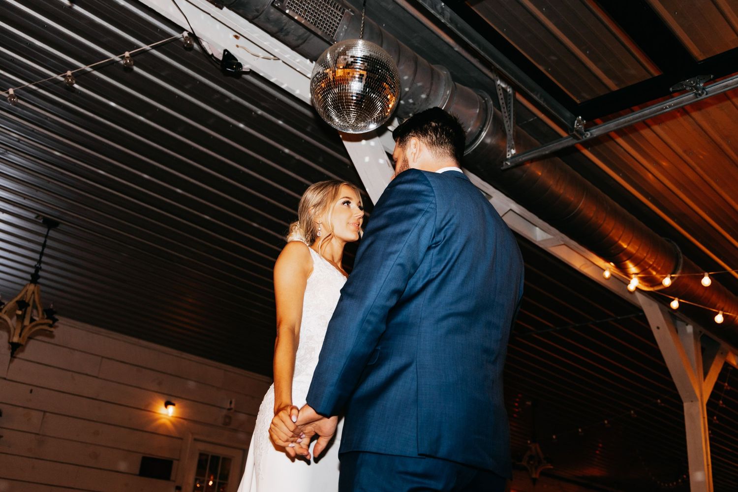 Bride and groom share a romantic slow dance under a disco ball at their wedding reception.