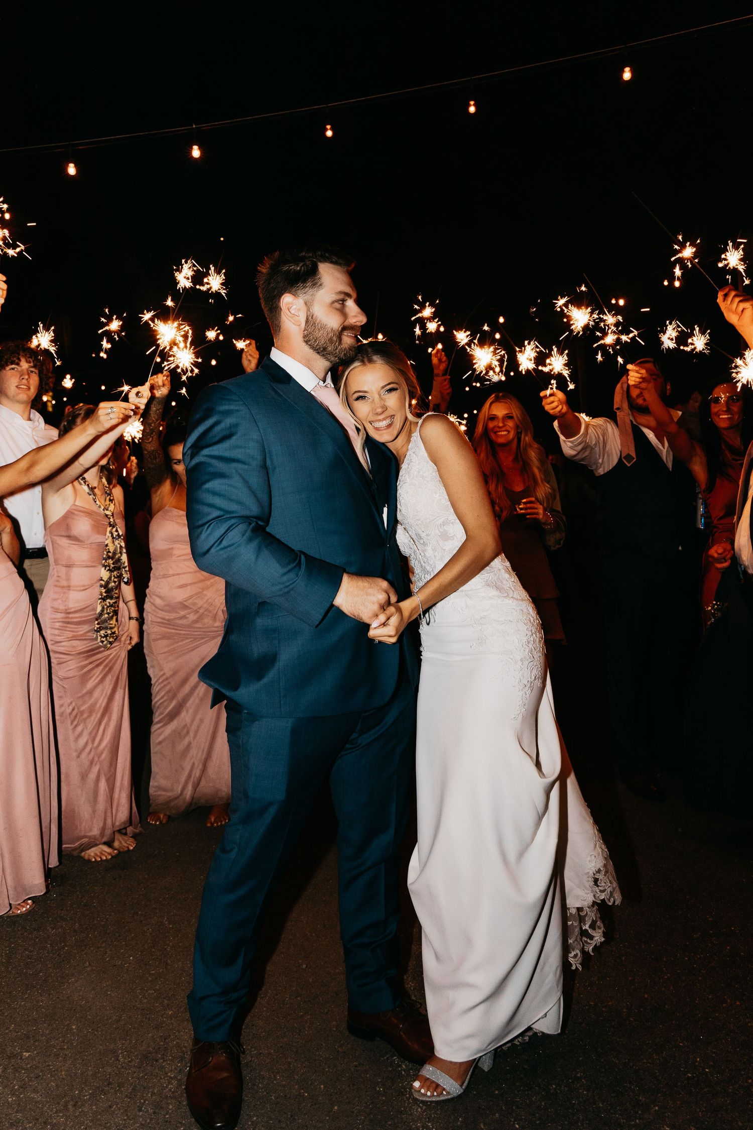 Bride and groom walk through a sparkling sparkler exit surrounded by cheering wedding guests.