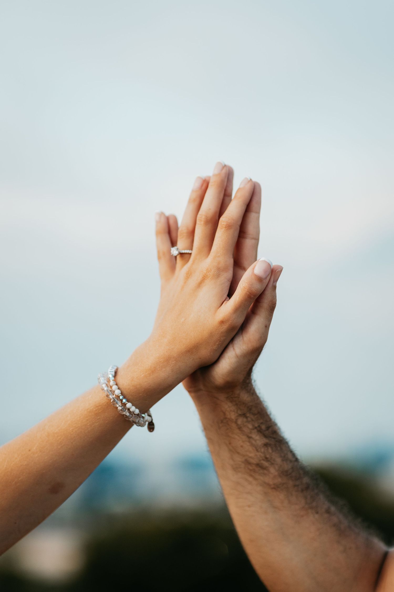 Close-up of an engaged couple pressing their hands together palm-to-palm showing an engagement ring and bracelet.