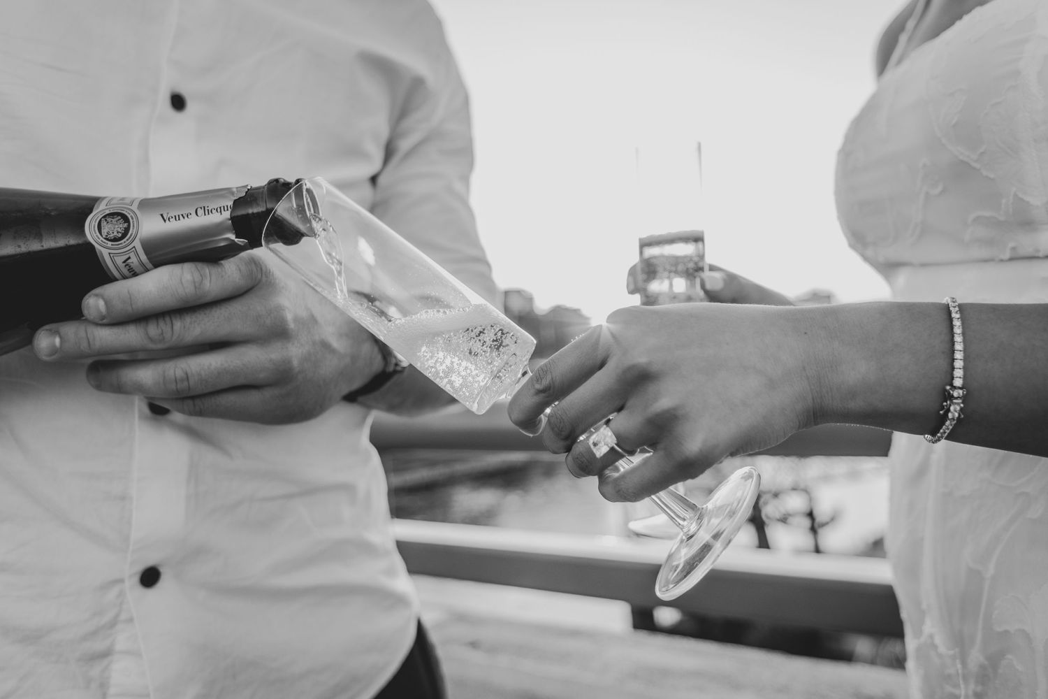 Black and white photo of a couple pouring champagne into a glass during a celebration.