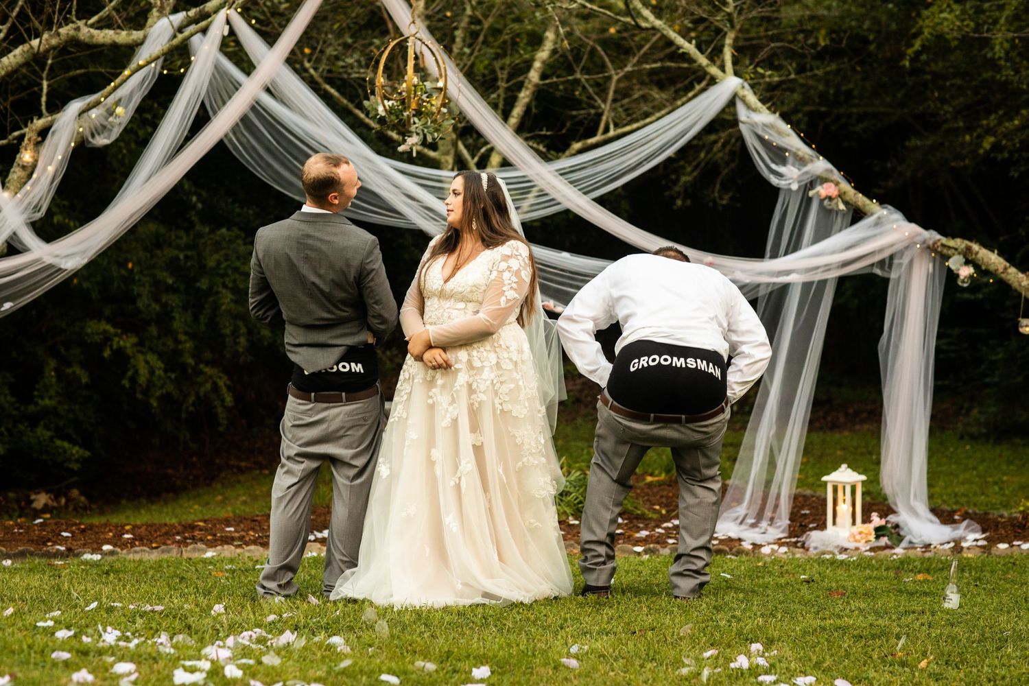 Bride and groom standing at outdoor wedding altar decorated with flowing gray draping and greenery.