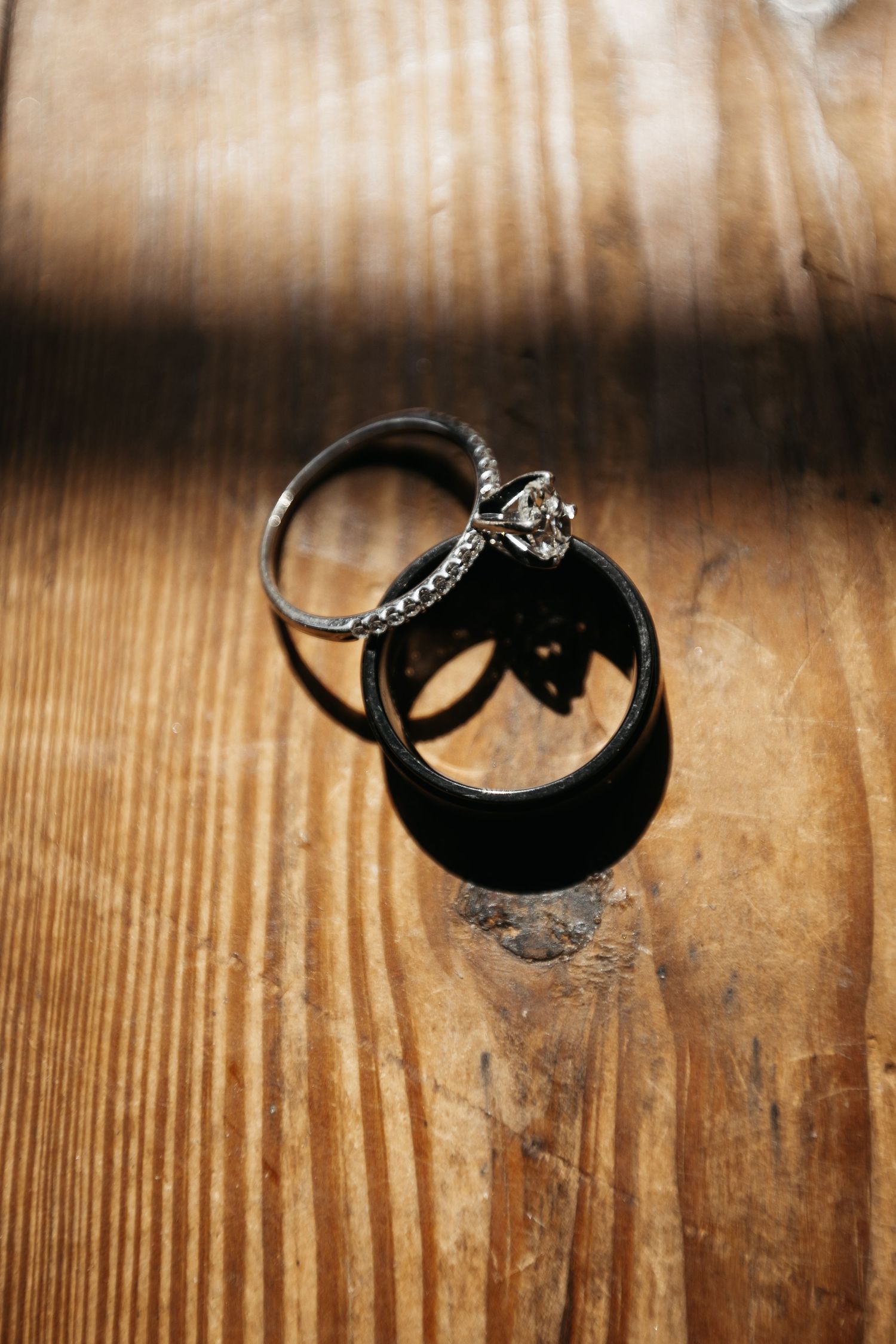 Wedding rings casting shadows on a rustic wooden surface in natural light.