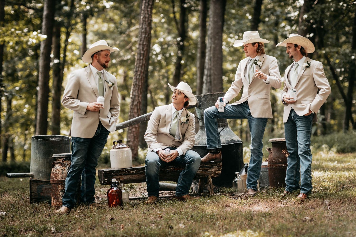 Four groomsmen in cowboy hats relaxing together in a rustic woodland setting.
