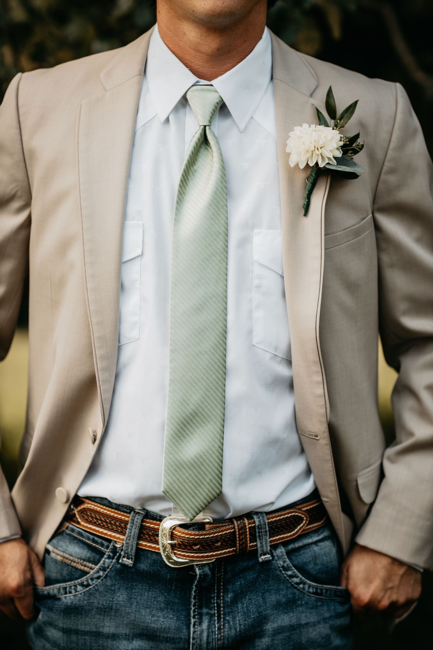 Groom wearing a tan blazer, mint tie, jeans, and floral boutonniere at a country wedding.