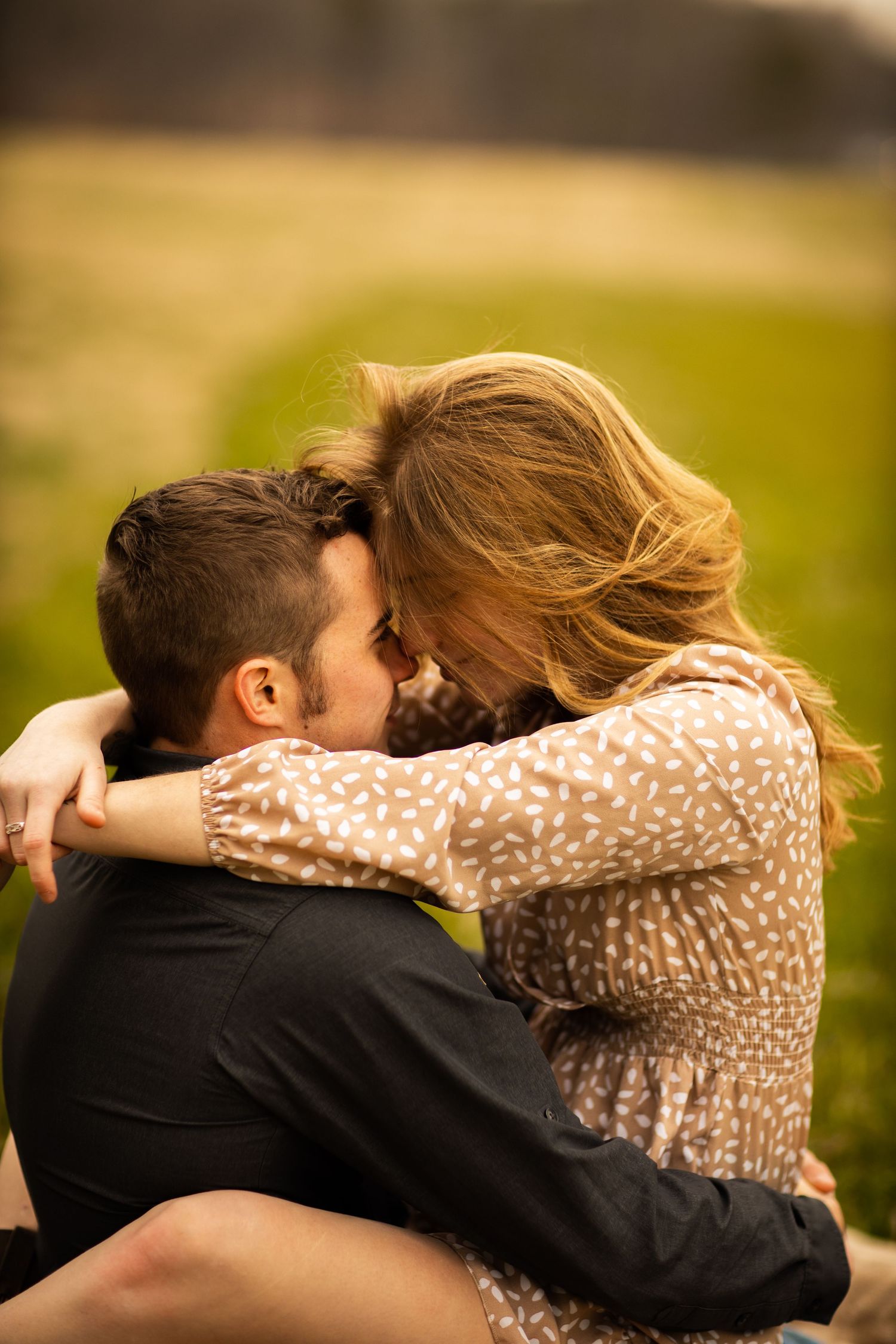 Couple embracing and laughing together while sitting in a golden sunlit green field.