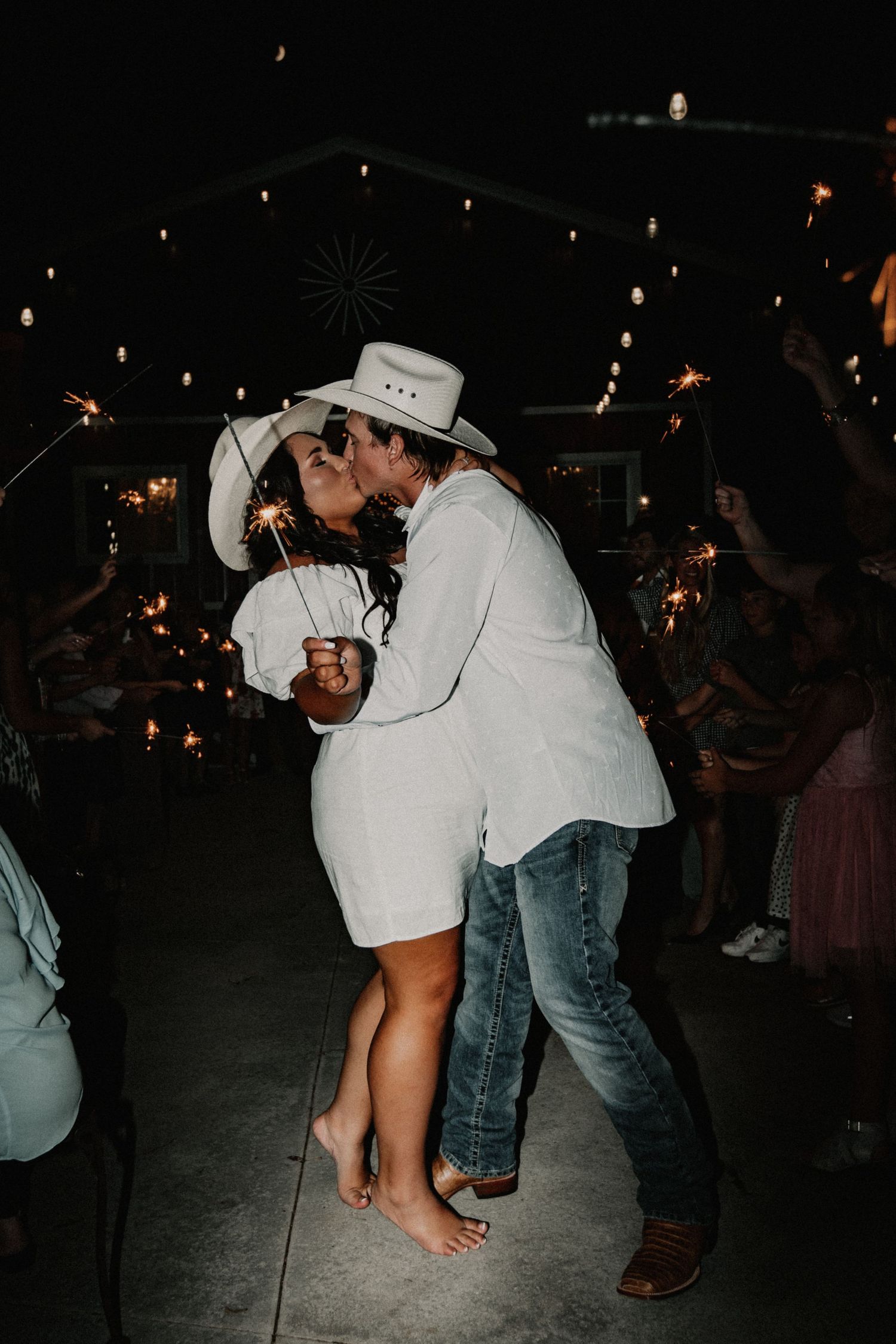 Two women dancing energetically at a wedding reception in a rustic barn venue.