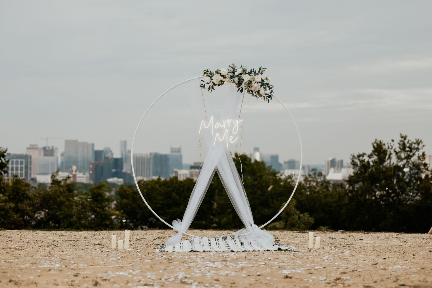 Elegant circular wedding arch with white draping and floral crown against city skyline.
