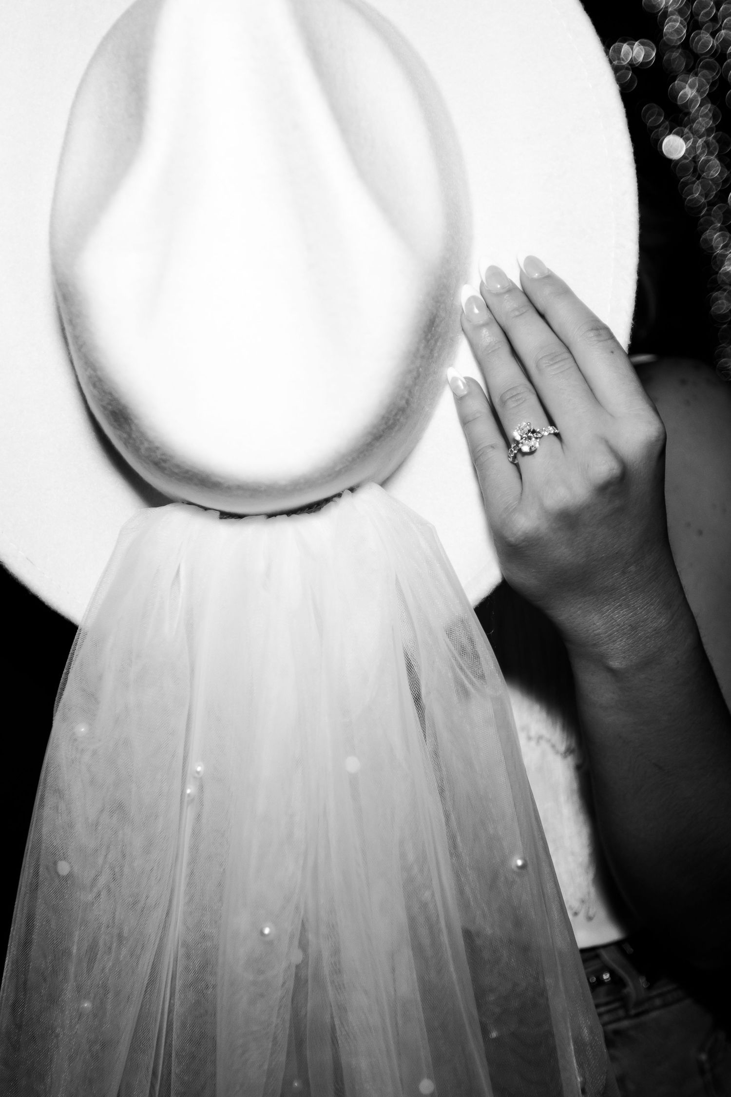 Black and white photo of bridal hat with veil and diamond engagement ring.
