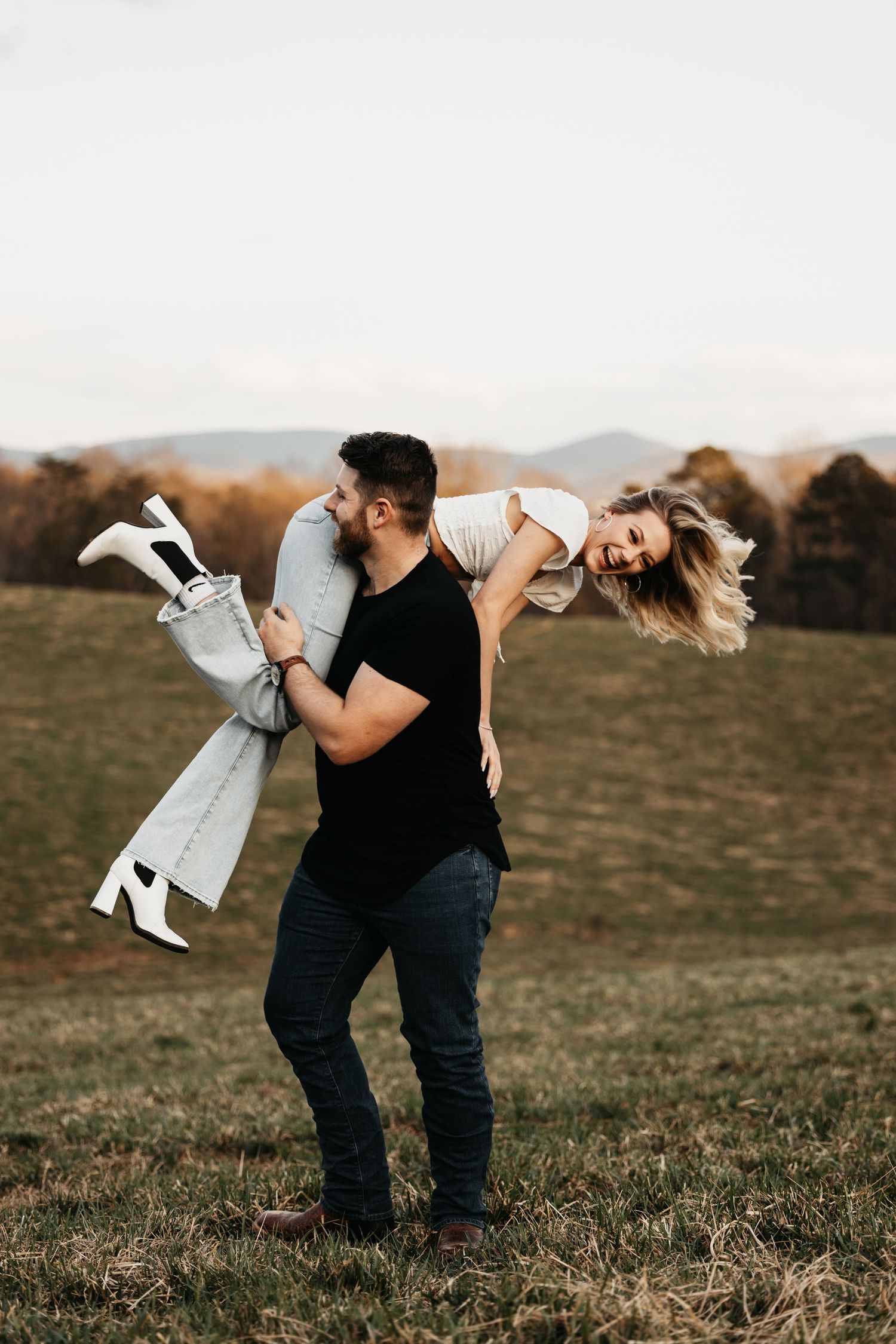 Man playfully carrying laughing woman over his shoulder in an open field.