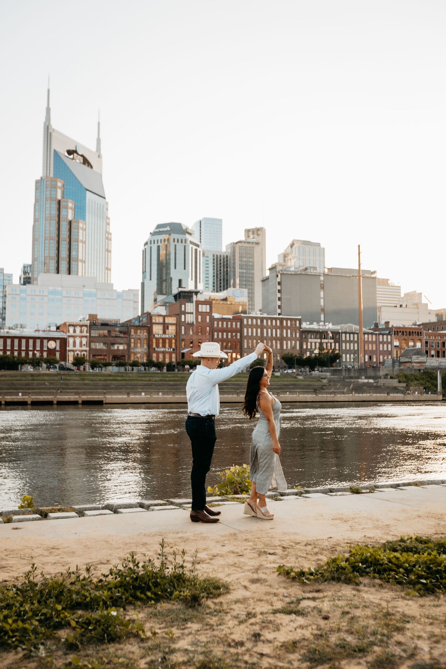 Couple dancing along the Cumberland River with the Nashville city skyline at golden hour.