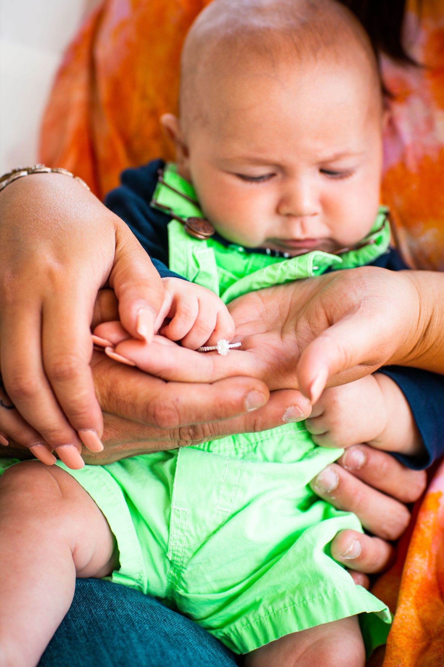 Parents cradling newborn baby in green outfit while gently holding tiny hands together.