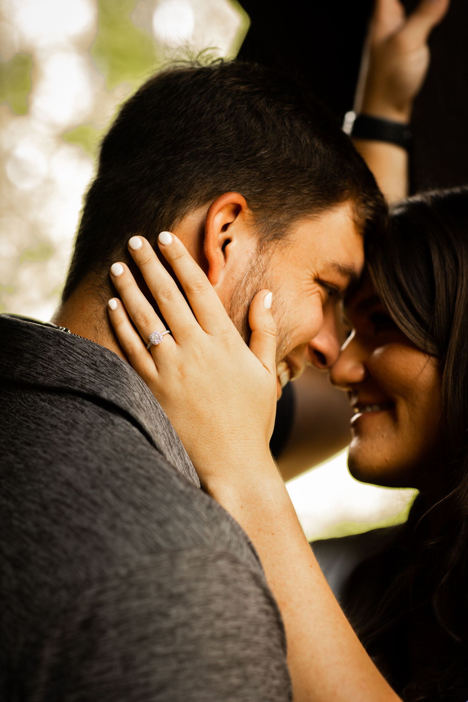 Engaged couple sharing a tender forehead-to-forehead moment, woman wearing a diamond ring on her hand.