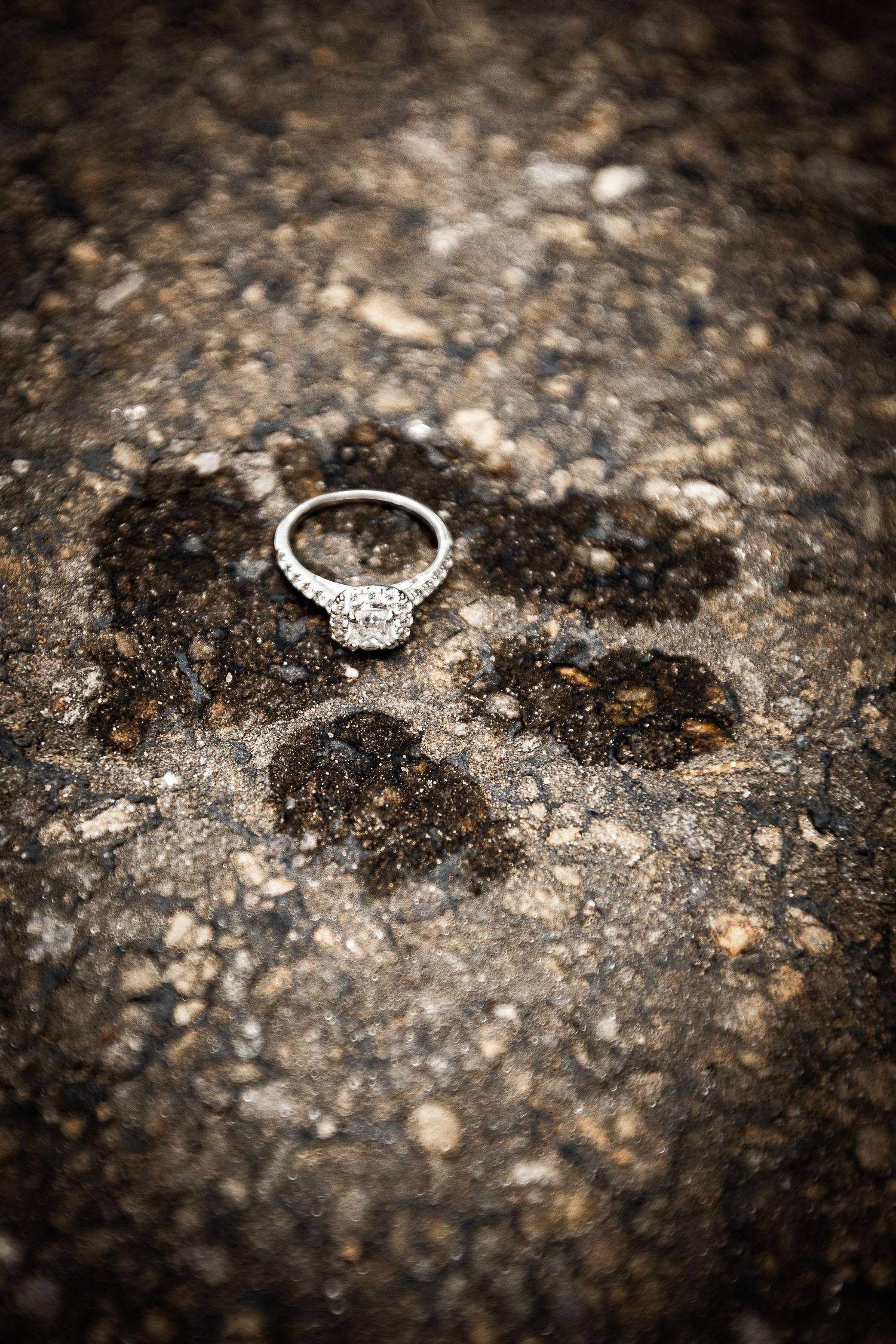 Diamond engagement ring resting on a textured stone surface with a bokeh background.