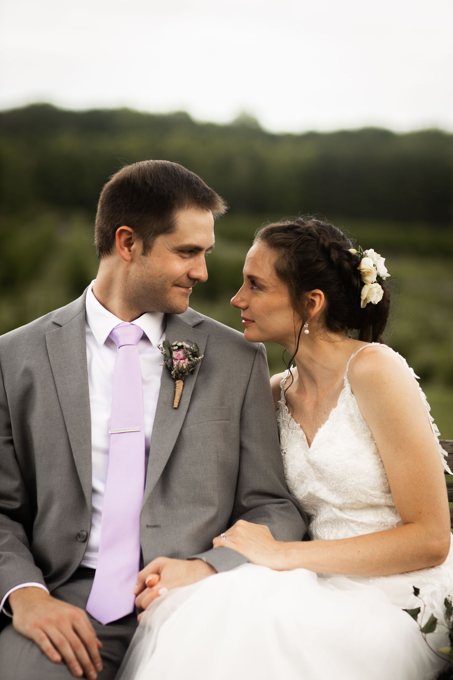 Bride and groom in gray suit with lavender tie sharing a romantic moment while seated outdoors.