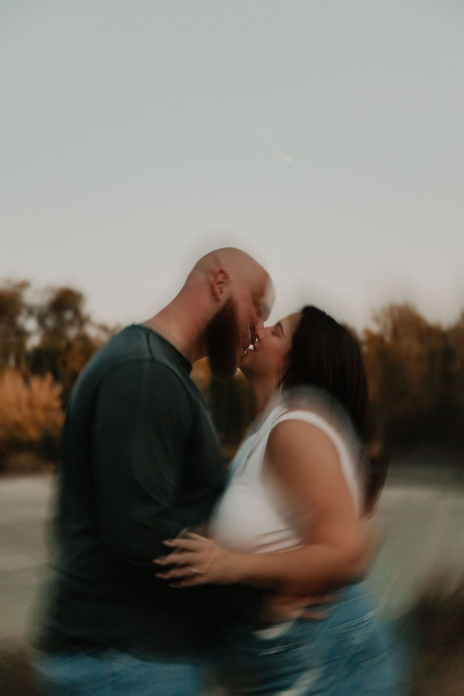 Couple sharing a romantic blurry kiss outdoors at golden hour near a lake.