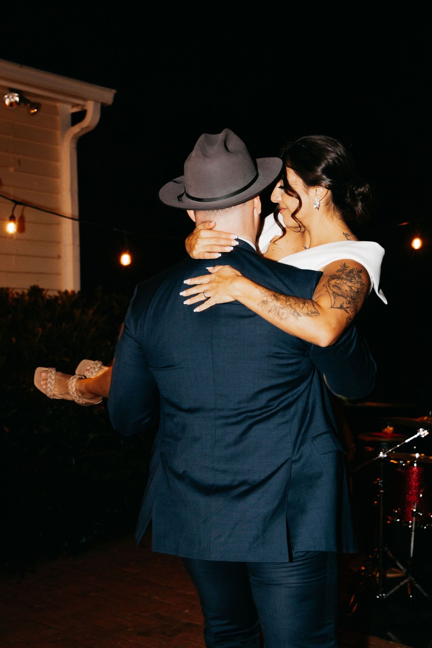 Couple sharing a romantic first dance outdoors at night under string lights at a wedding reception.
