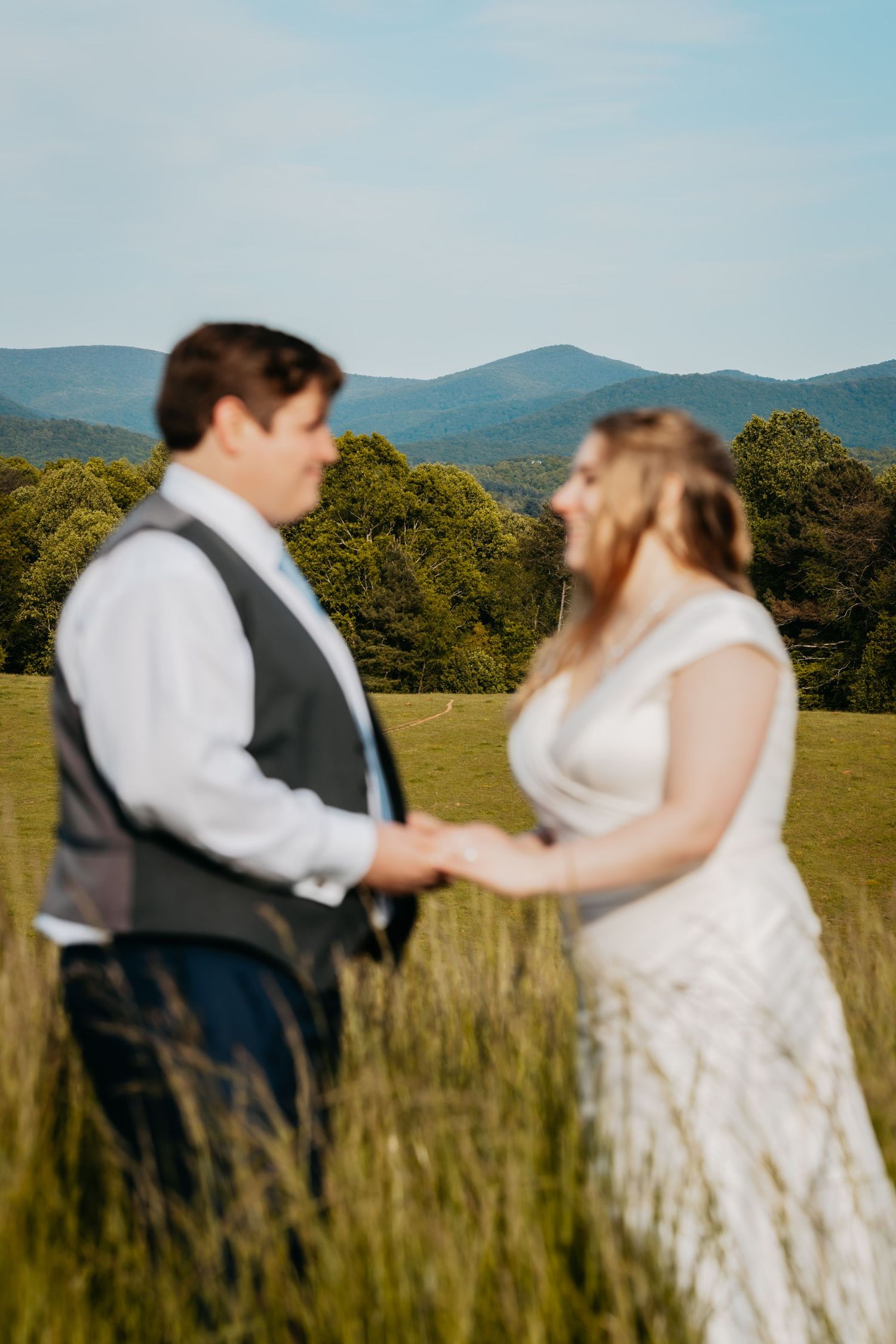 Blurred bride and groom hold hands in a tall grass field with mountain views behind them.