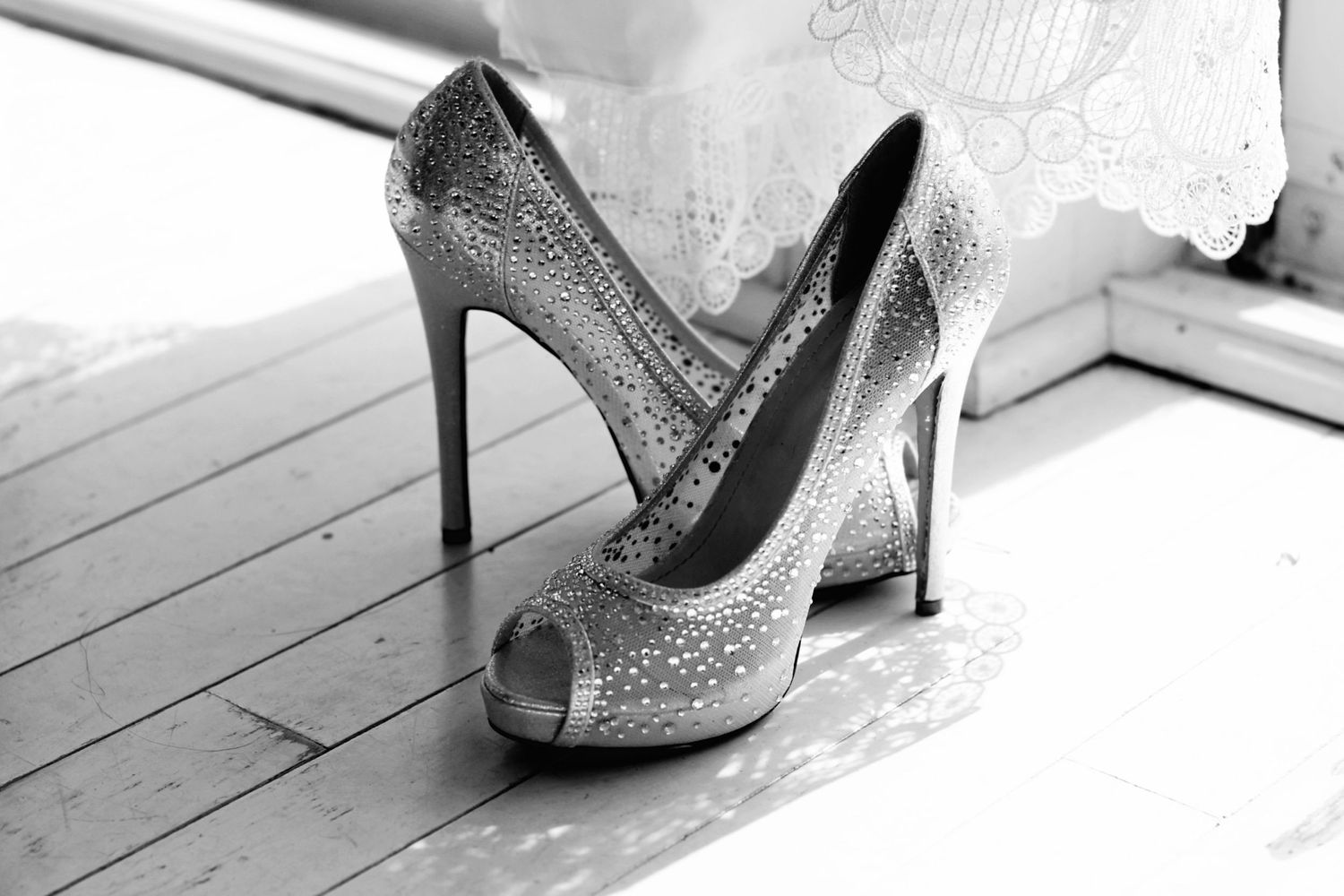 Black and white photo of sparkling crystal peep-toe bridal heels on a wooden floor.