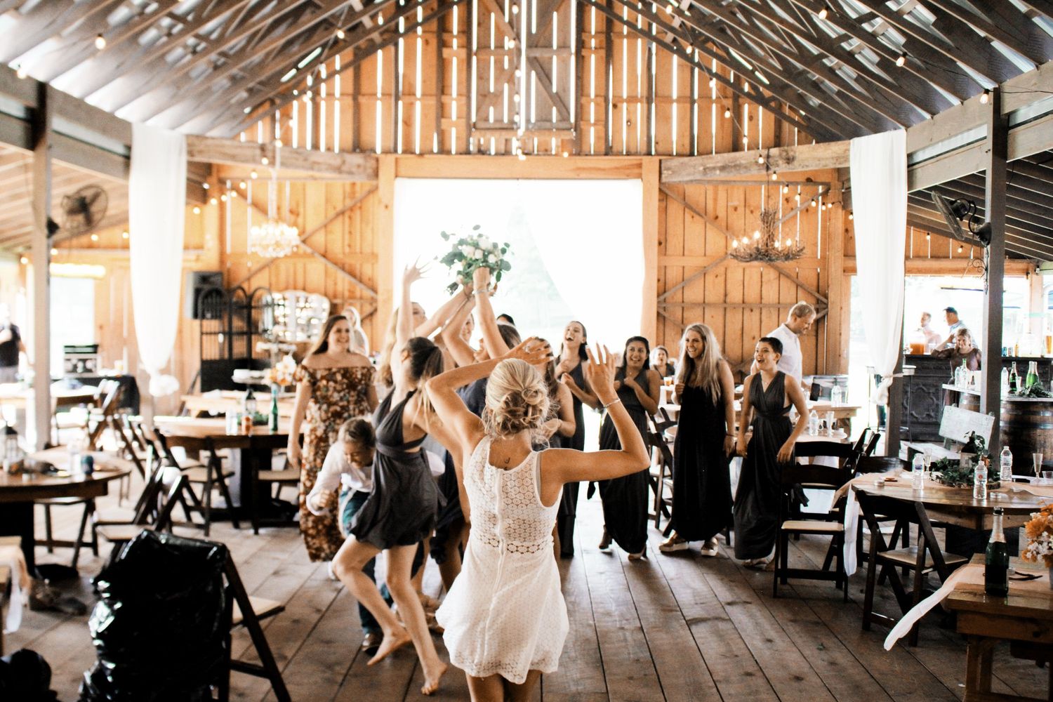 Bride dancing with guests in a rustic barn wedding reception with string lights.