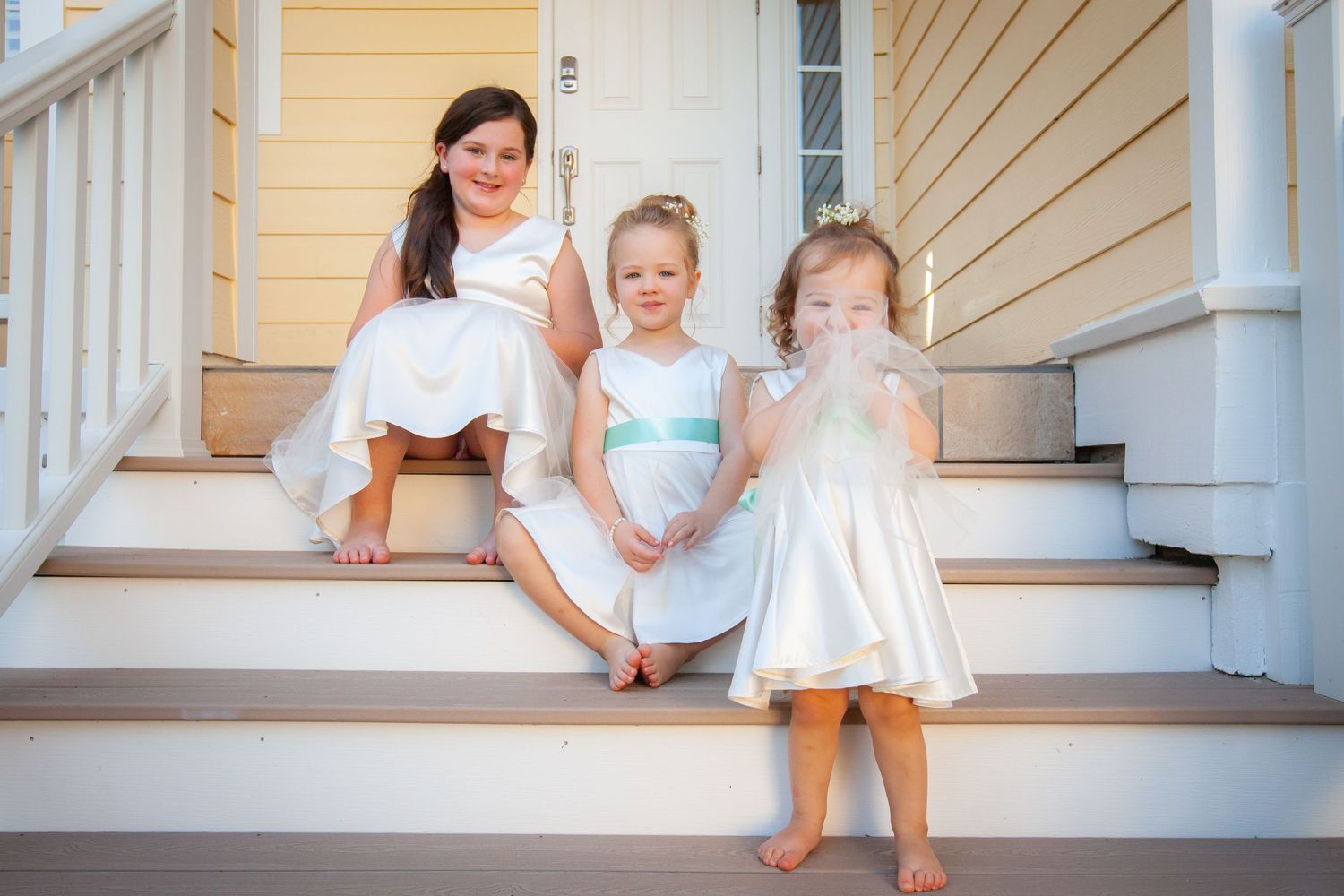 Three young girls in white dresses sitting on porch steps at a wedding.