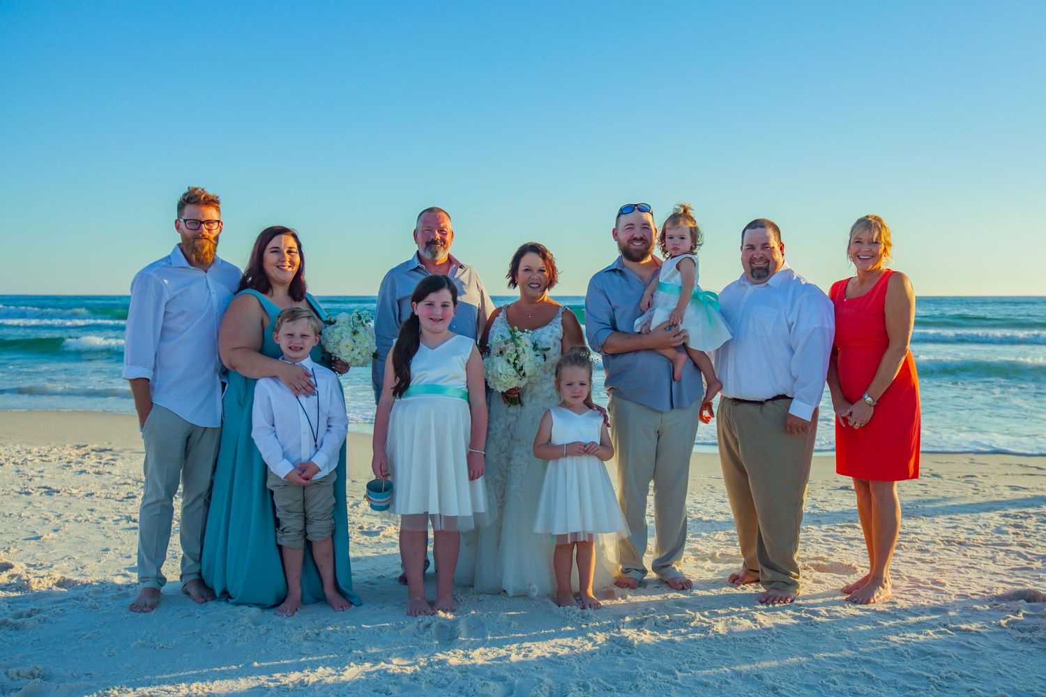 Large family group portrait on a sandy beach at sunset during a wedding celebration.