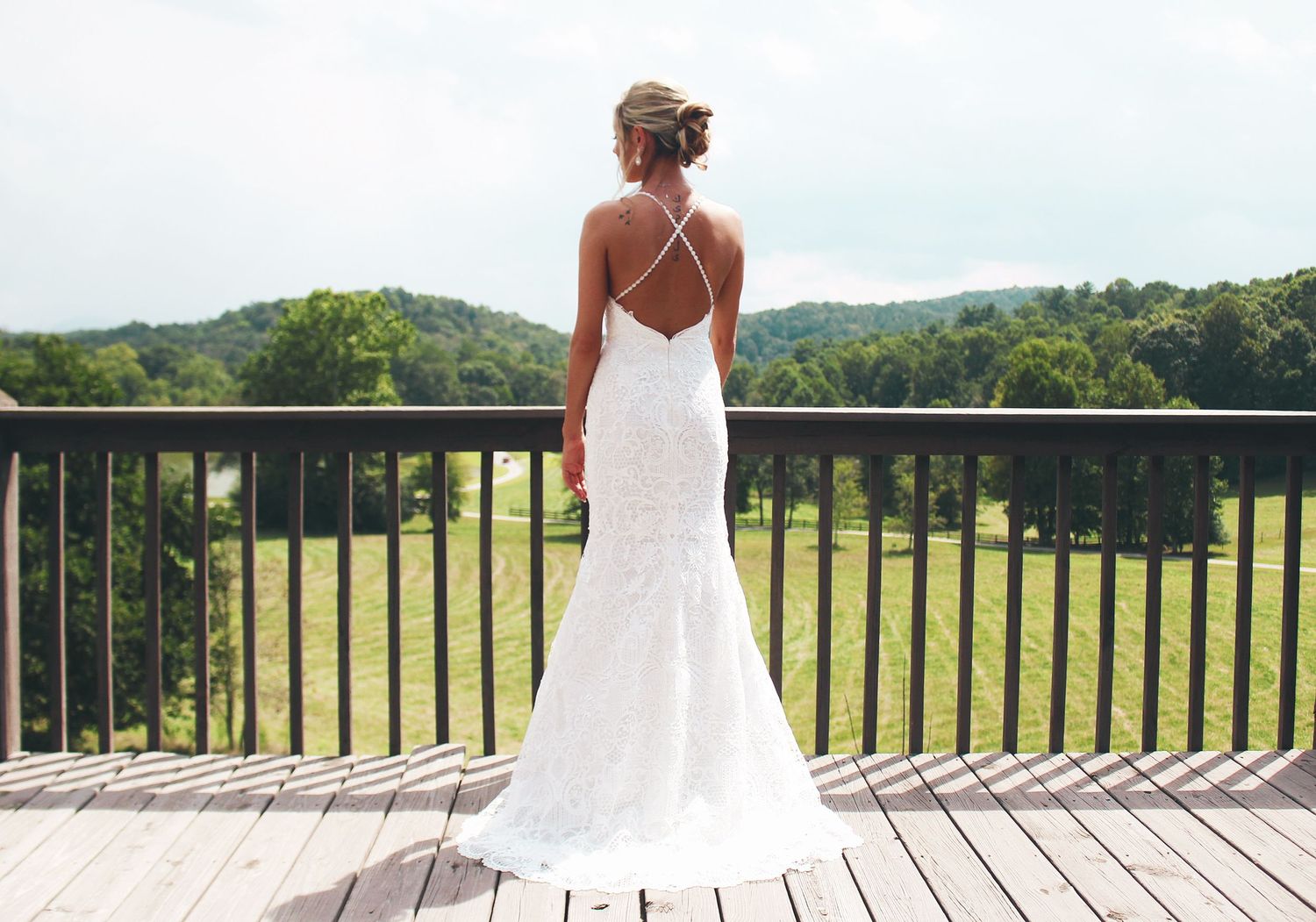 Bride in a backless lace mermaid wedding gown standing on a deck overlooking green hills.