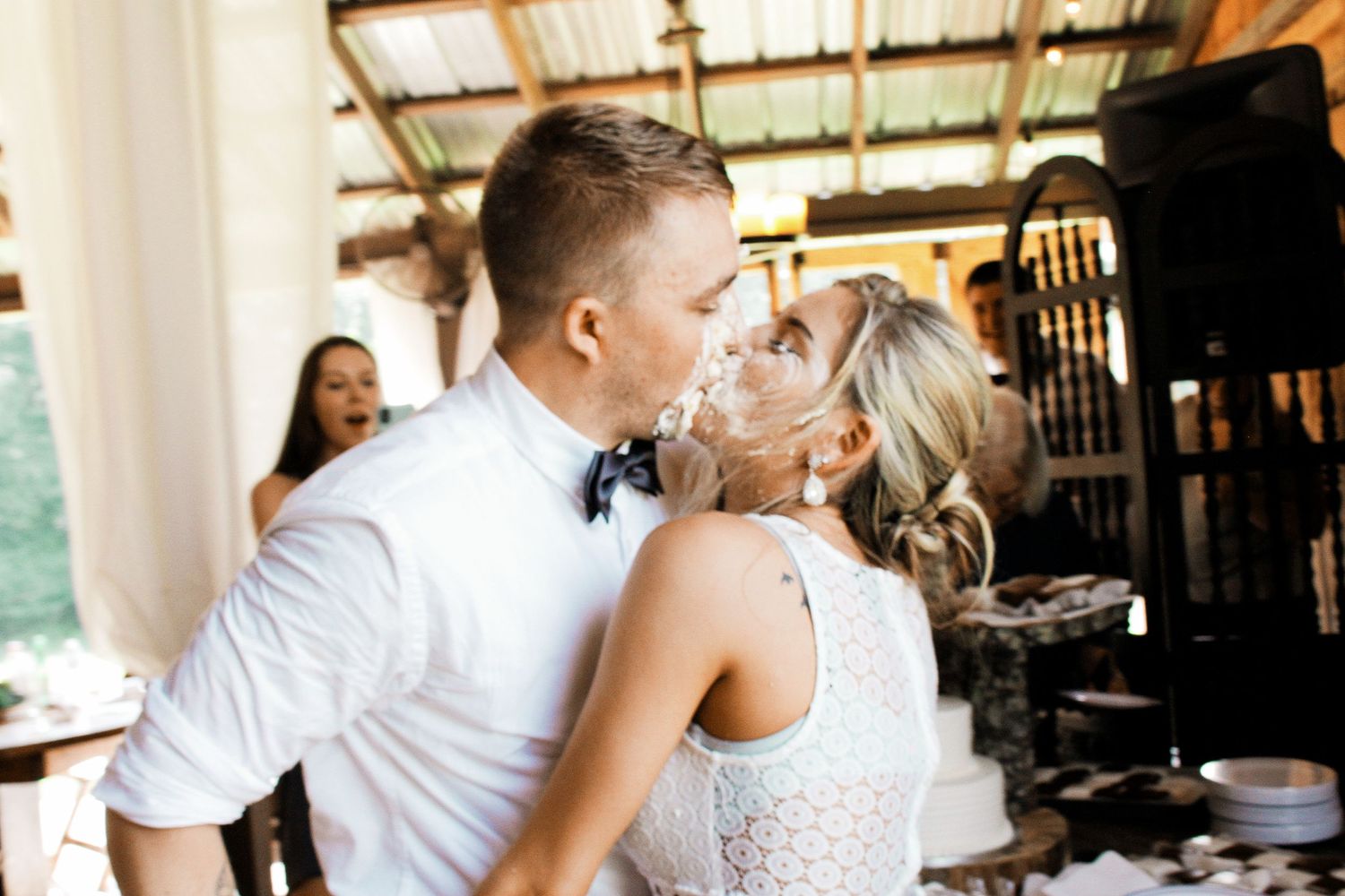 Bride and groom sharing a joyful cake smash moment at their rustic wedding reception.