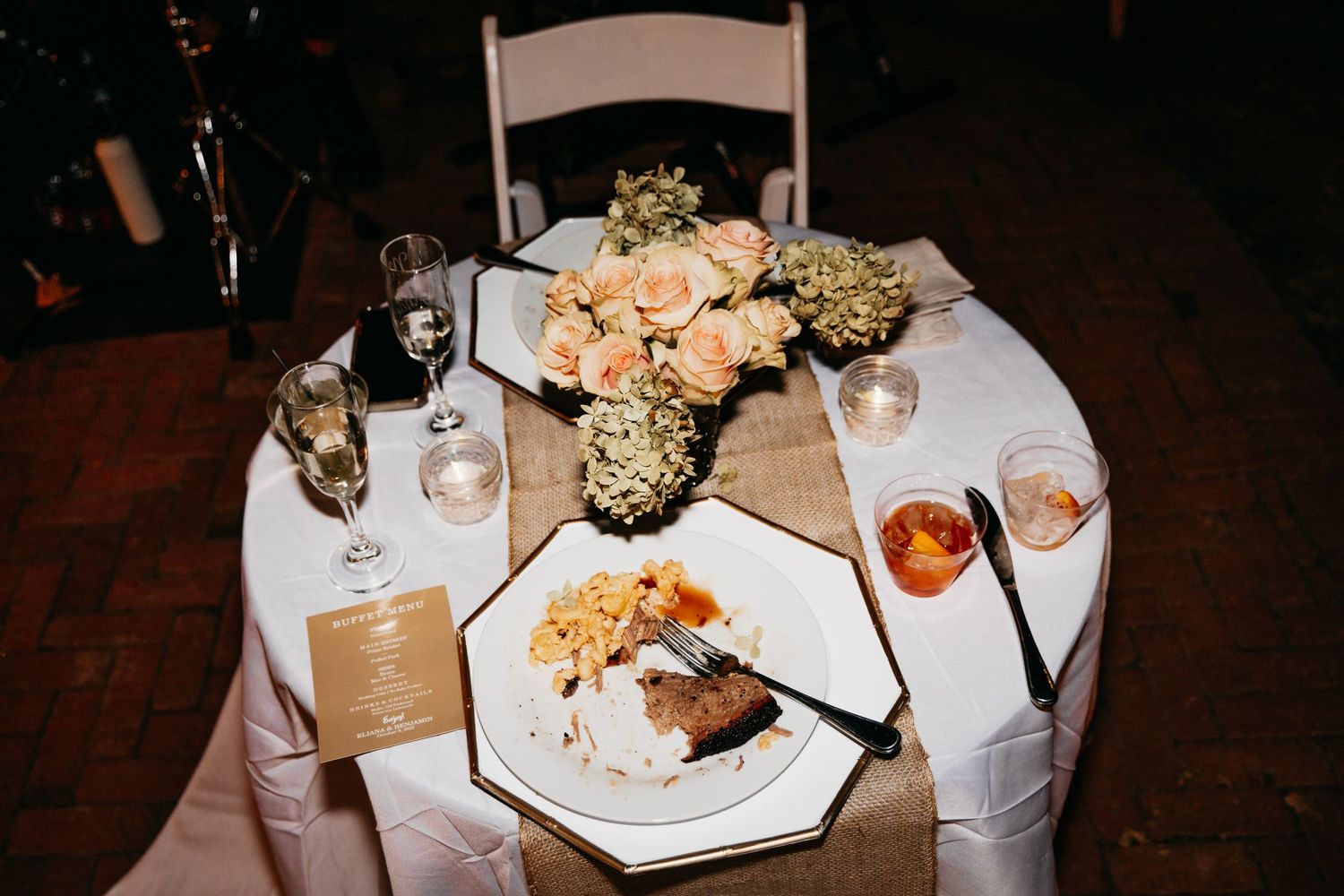 Elegant wedding reception table setting with peach roses, champagne glasses, and a plated dinner meal.