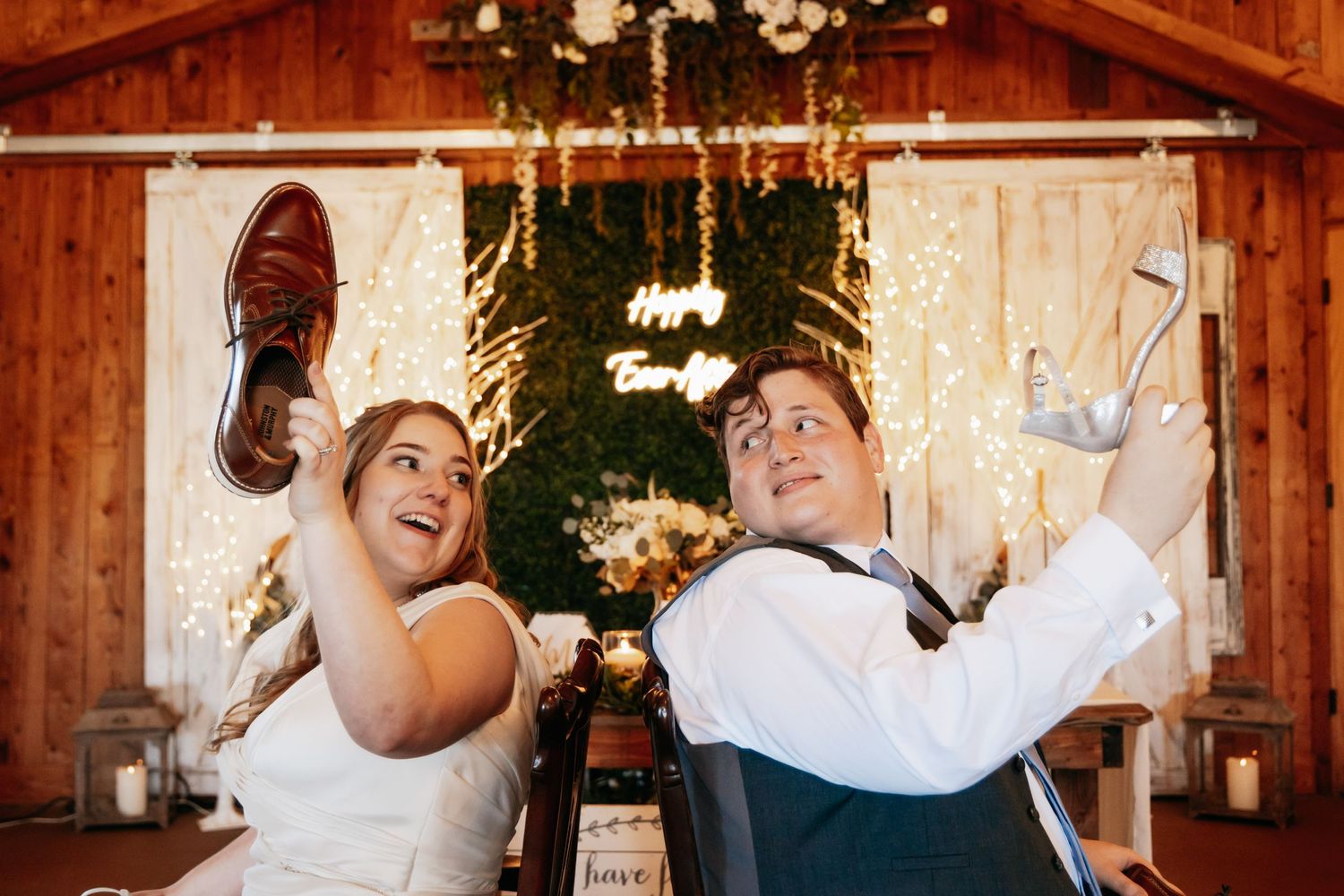 Bride and groom playfully hold up each other's shoes during a fun wedding reception game.
