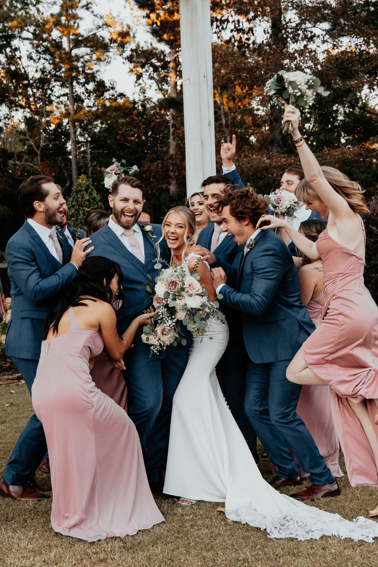 Bride and groom celebrate with cheering wedding party in navy suits and pink dresses.