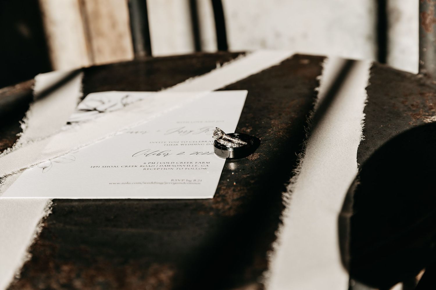 Wedding invitations and diamond rings arranged on a rustic surface with dramatic light and shadow.