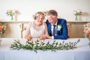 Bride and groom sign the register. They are laughing and sitting close together.