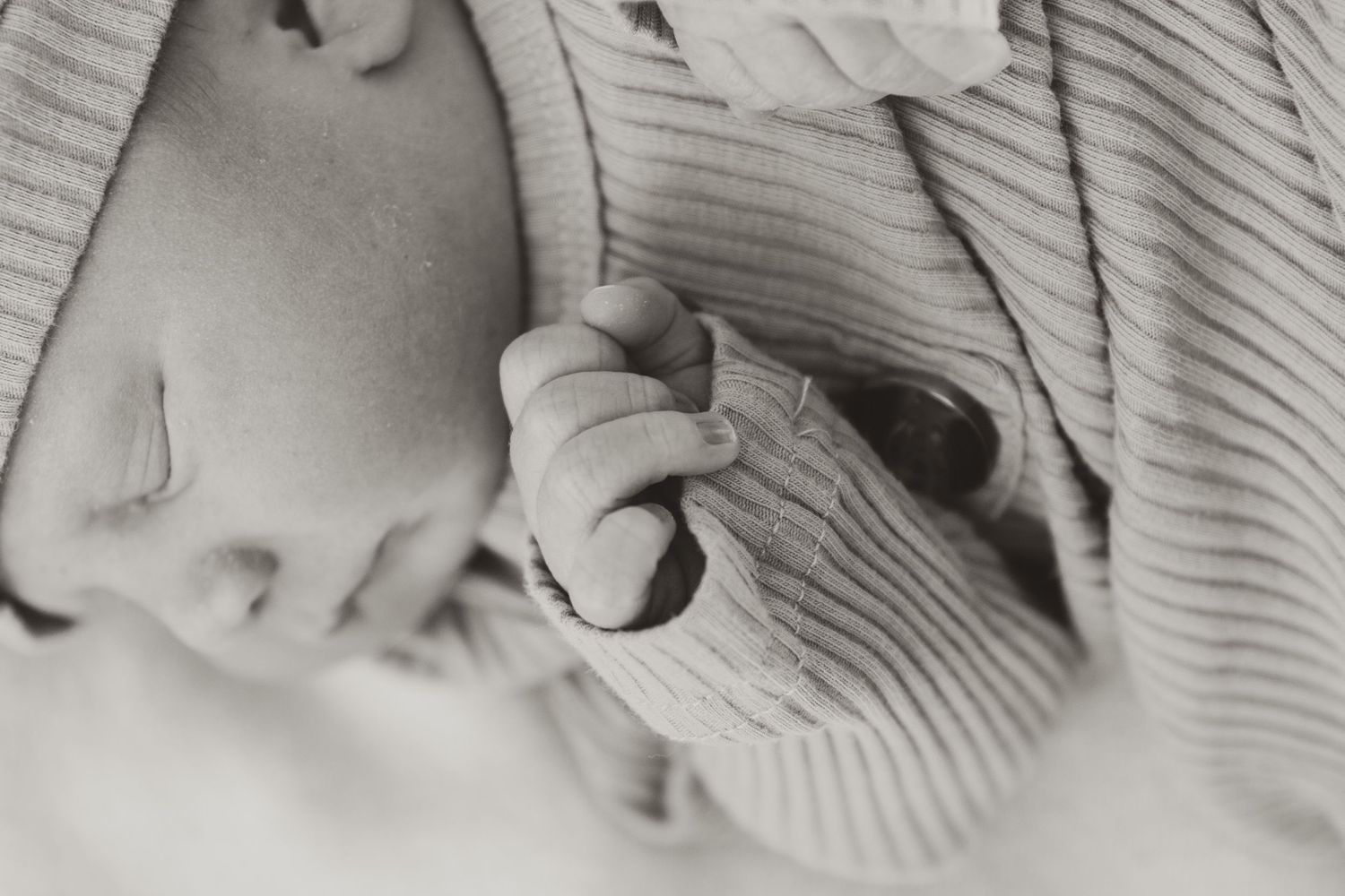 Black and white closeup of a sleeping baby's hand grasping fabric.