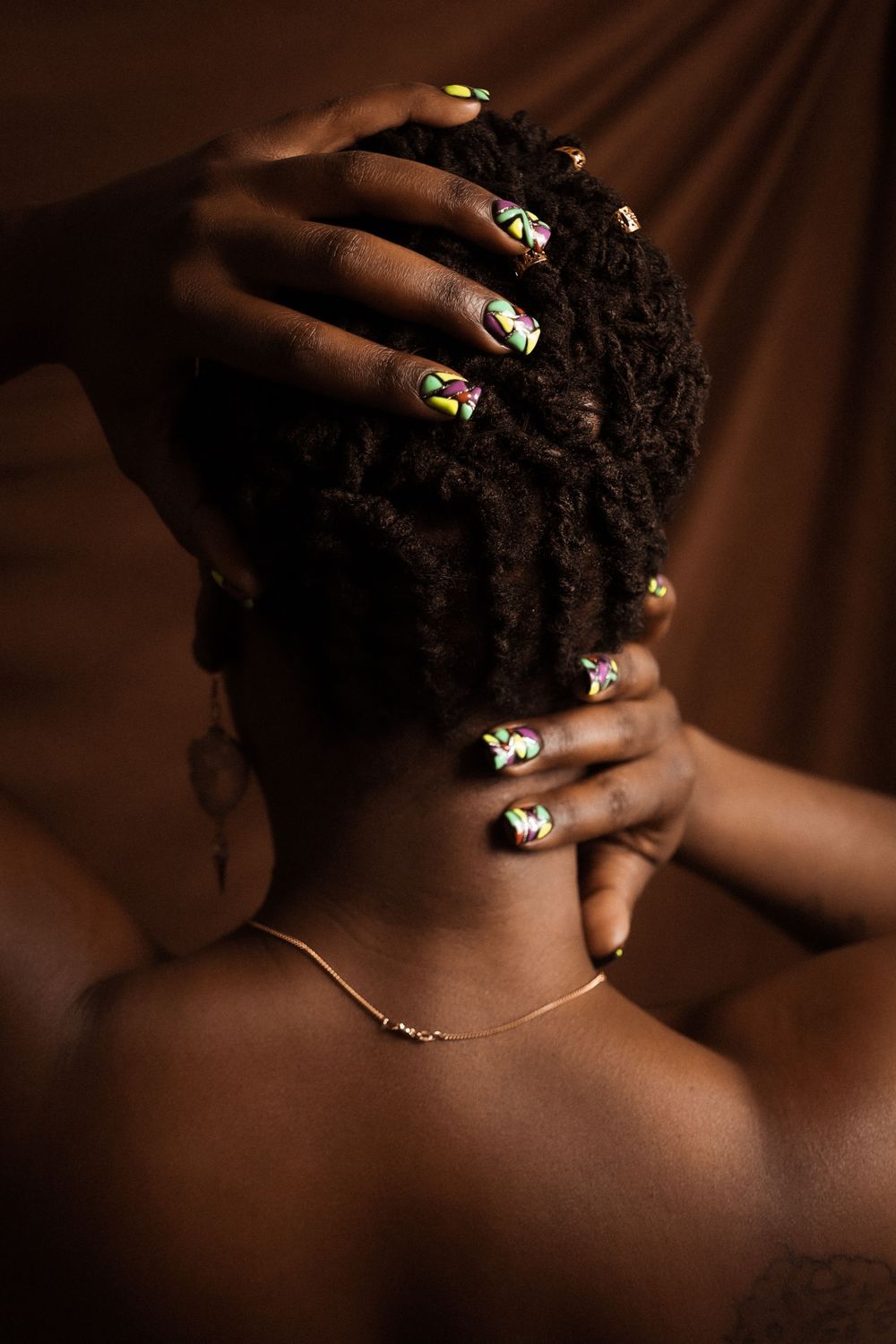Artistic photo showing decorated nails and jewelry against warm-toned background.