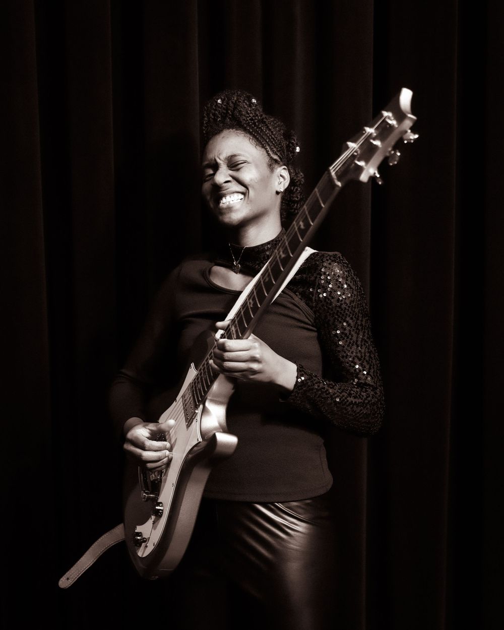 Joyful musician performing with an electric guitar on stage in monochrome.